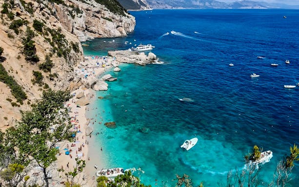 Trekking along Cala Mariolu's rocky coastline with turquoise waters and boats.