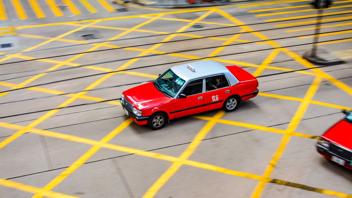 Red taxi driving through a busy intersection in Hong Kong.