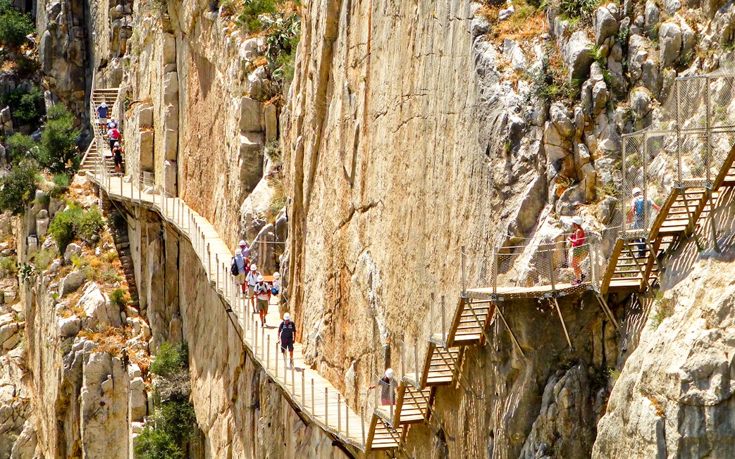 Hikers on Caminito del Rey walkway along steep cliffs in Malaga, Spain.