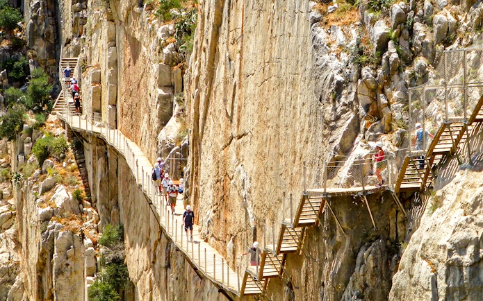 Hikers on Caminito del Rey walkway along steep cliffs in Malaga, Spain.