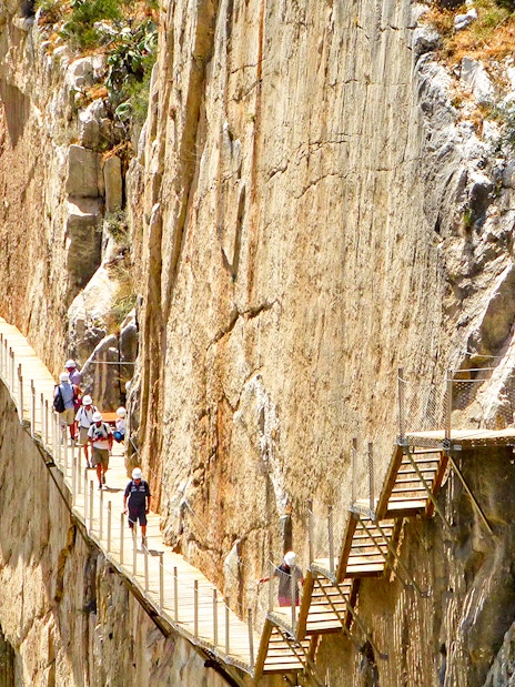 Hikers on Caminito del Rey walkway along steep cliffs in Malaga, Spain.