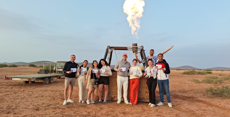 Tour group in Marrakech holding certificates after hot air balloon ride.