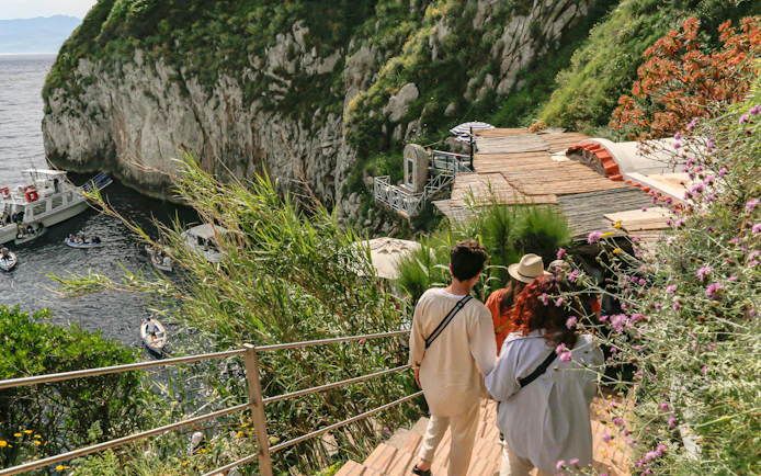 Tourists descend wooden stairs toward Blue Grotto entrance, Capri, Italy.