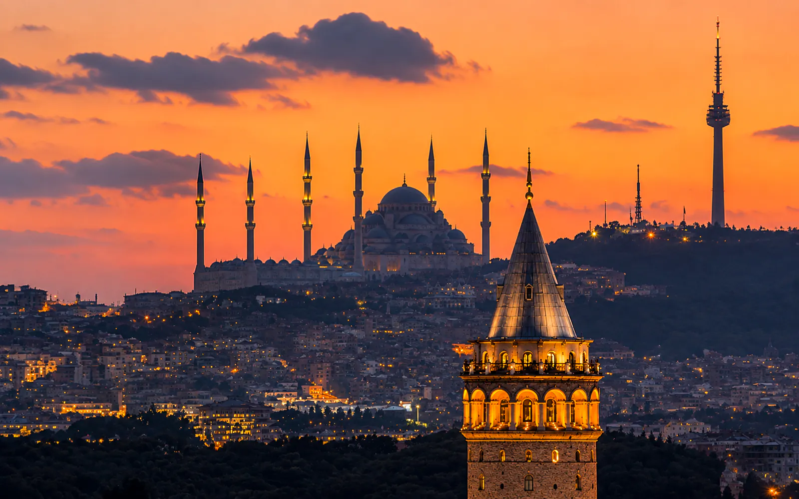 Galata Tower illuminated at sunset with Istanbul skyline in the background.