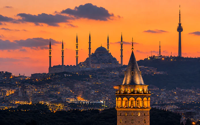 Galata Tower illuminated at sunset with Istanbul skyline in the background.