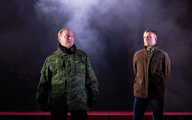 Two men in military and casual jackets stand on stage with smoke backdrop, related to Patriots.