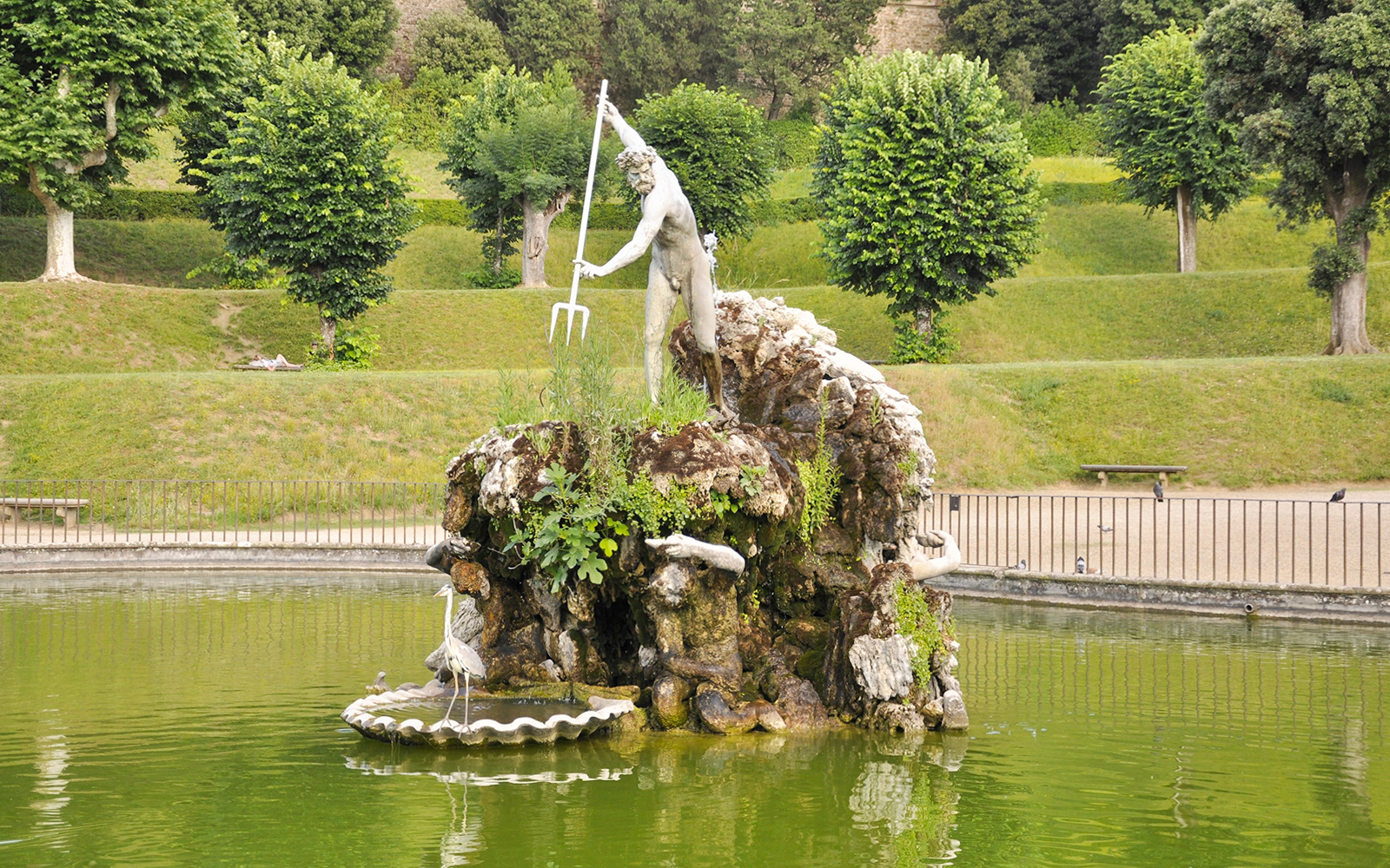 Statue of Neptune in Boboli Garden fountain, Florence, Italy, surrounded by greenery.