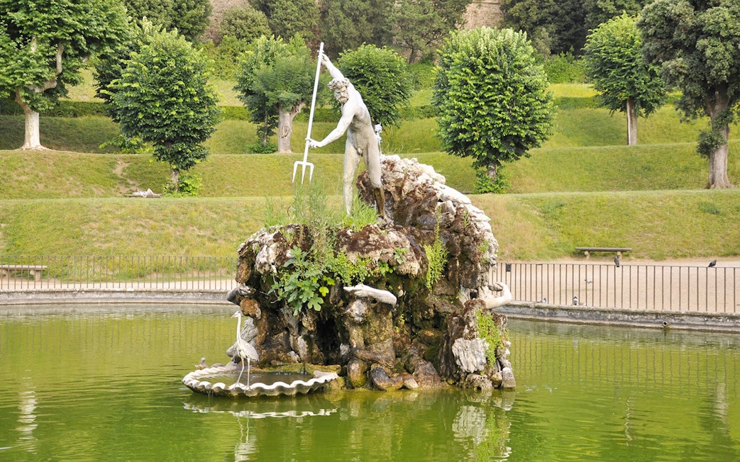 Statue of Neptune in Boboli Garden fountain, Florence, Italy, surrounded by greenery.