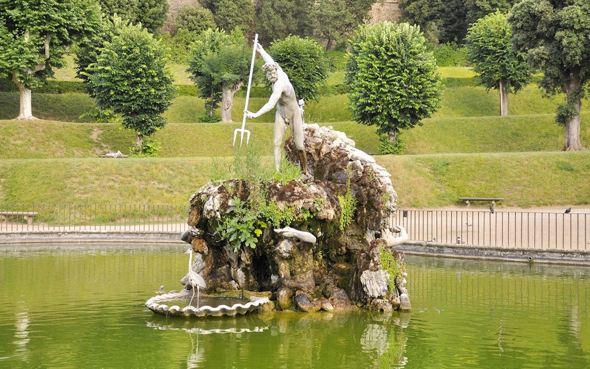 Statue of Neptune in Boboli Garden fountain, Florence, Italy, surrounded by greenery.