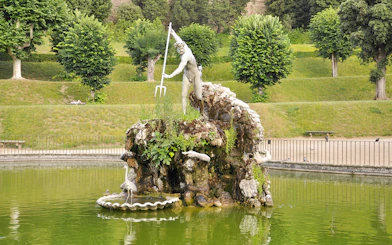 Statue of Neptune in Boboli Garden fountain, Florence, Italy, surrounded by greenery.