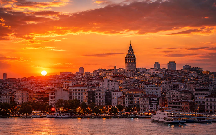 Galata Tower overlooking Istanbul skyline at sunset with vibrant sky.