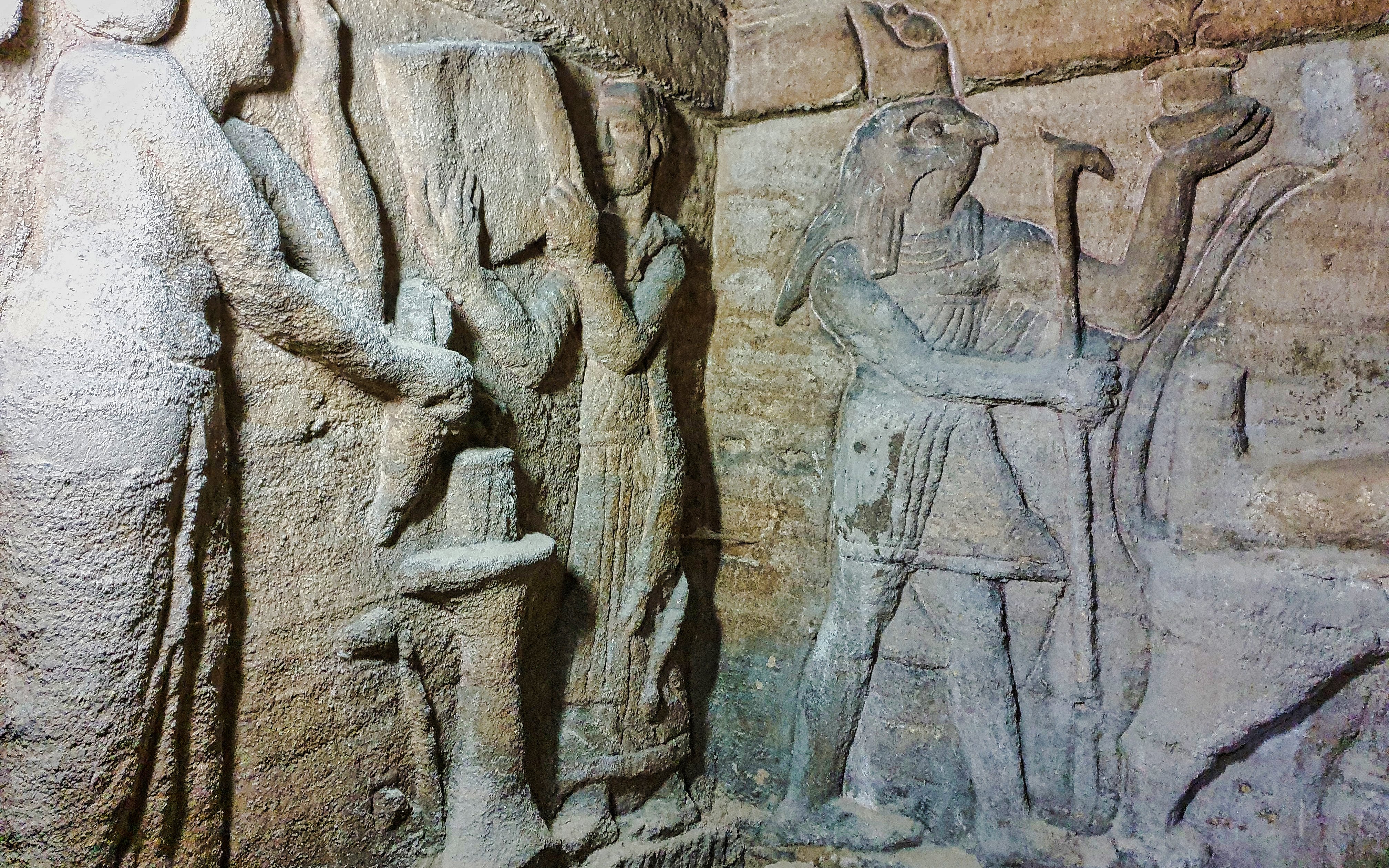 Priest and assistant preparing altar with Horus relief in Kom El Shoqafa catacombs.
