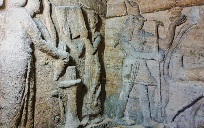 Priest and assistant preparing altar with Horus relief in Kom El Shoqafa catacombs.