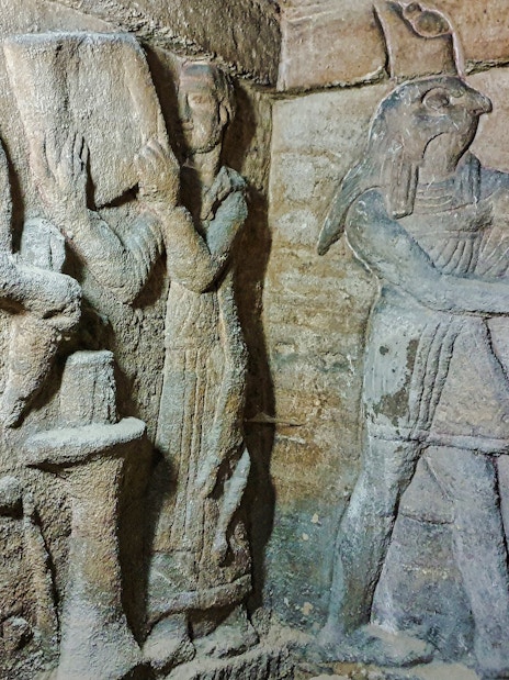 Priest and assistant preparing altar with Horus relief in Kom El Shoqafa catacombs.