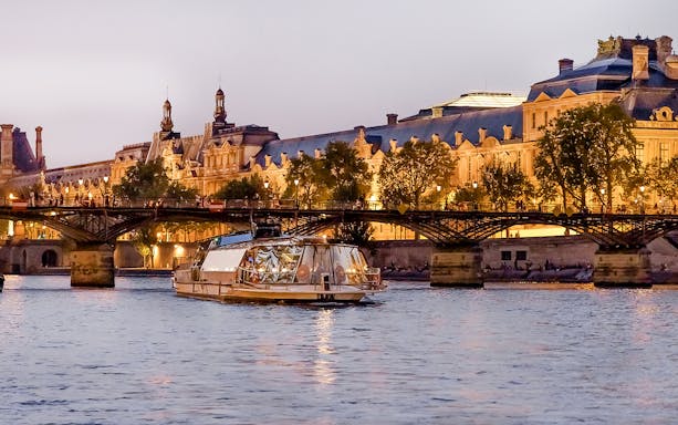 Bateaux Parisiens cruise on the Seine River with illuminated Parisian architecture in the background.