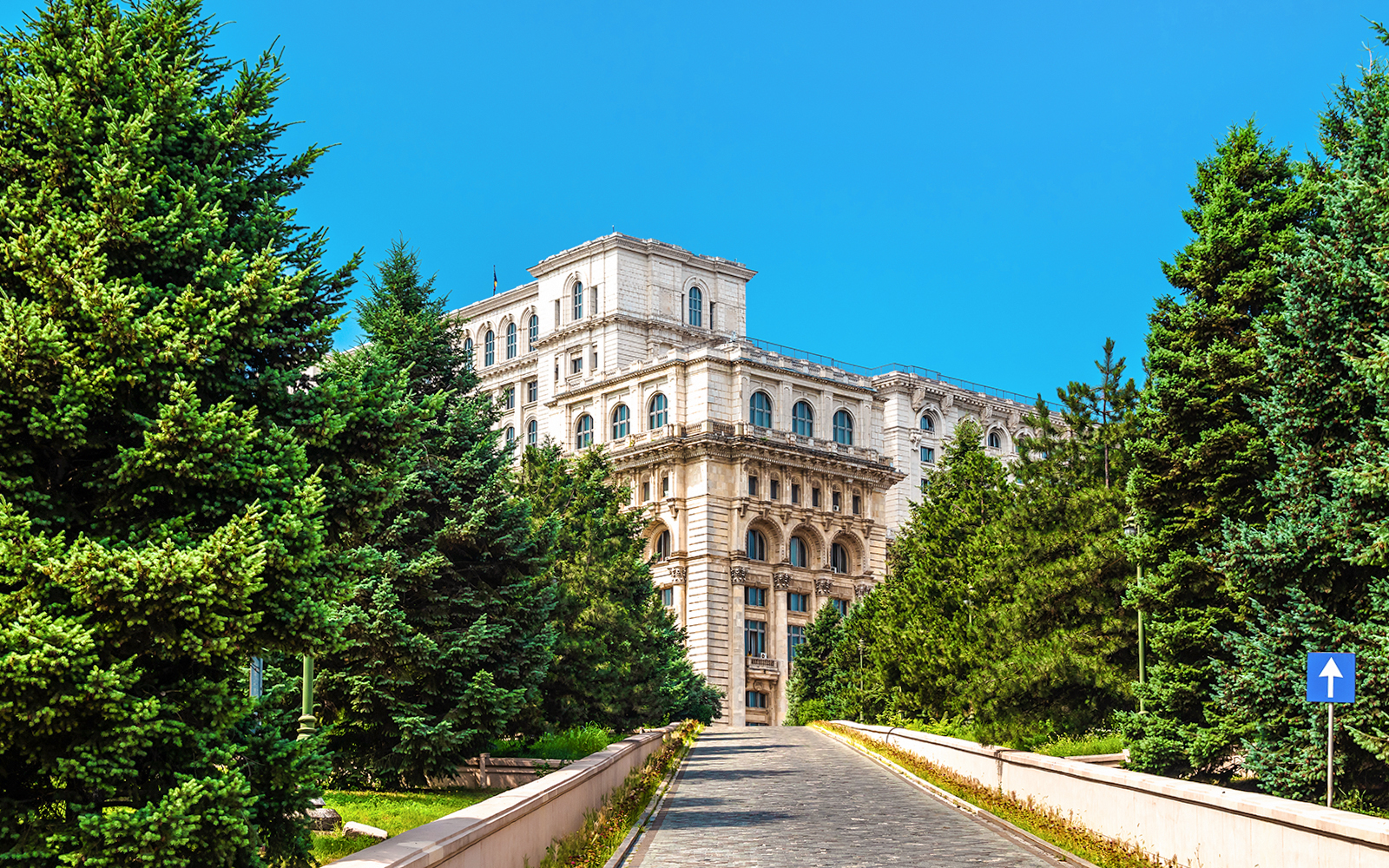 Palace of the Parliament in Bucharest surrounded by trees on a sunny day.