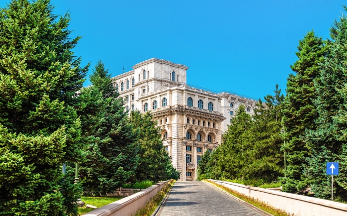 Palace of the Parliament in Bucharest surrounded by trees on a sunny day.