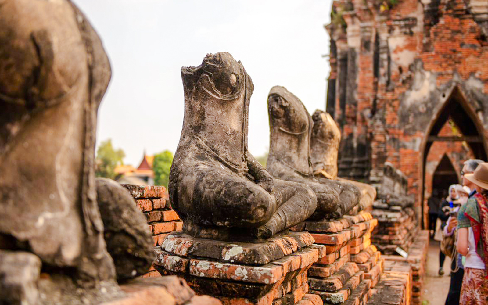 Seated Buddha statues at Wat Chaiwatthanaram, Ayutthaya, with tourists exploring the temple.