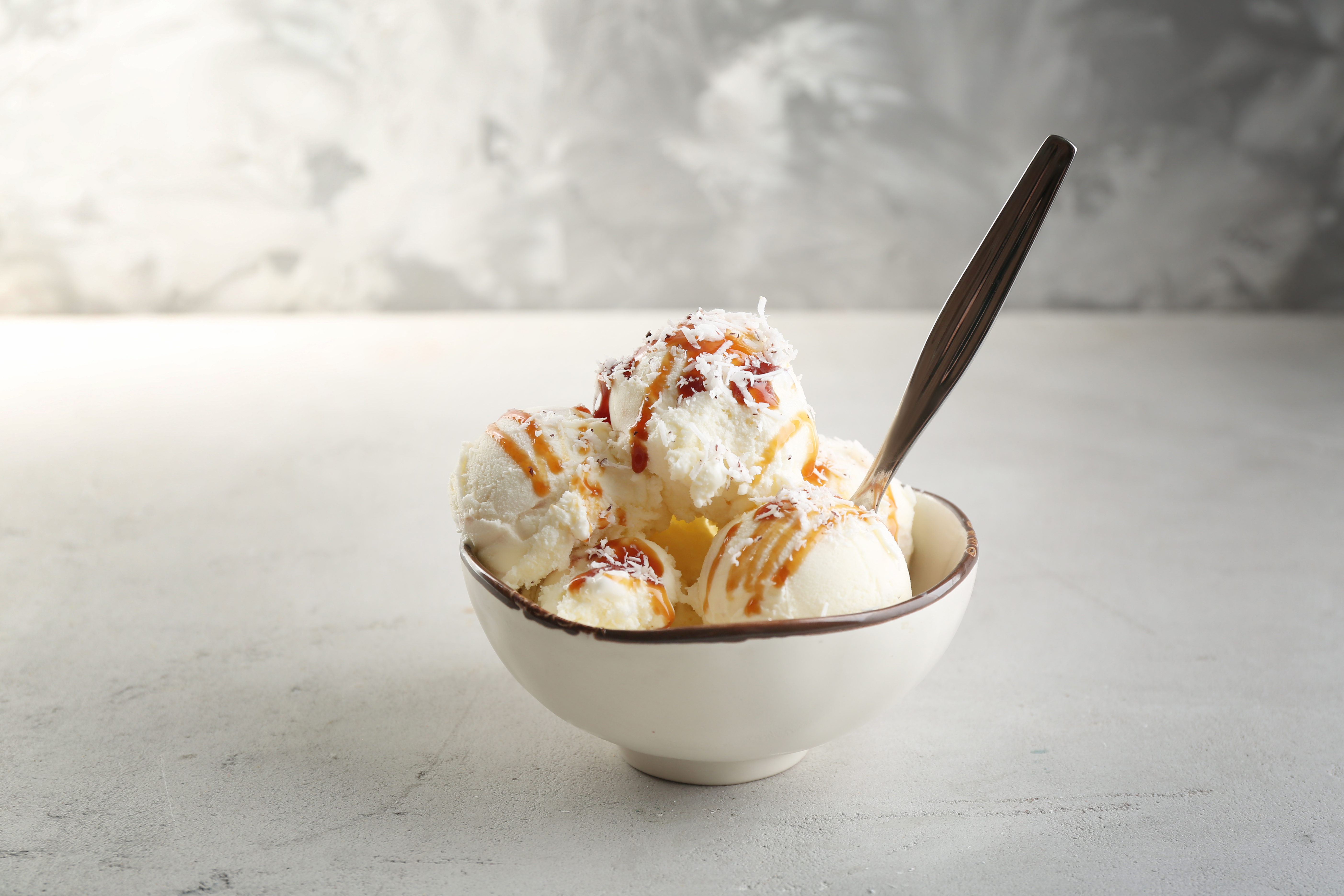 Coconut ice cream scoops in a bowl with syrup and shredded coconut.