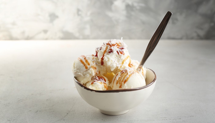 Coconut ice cream scoops in a bowl with syrup and shredded coconut.