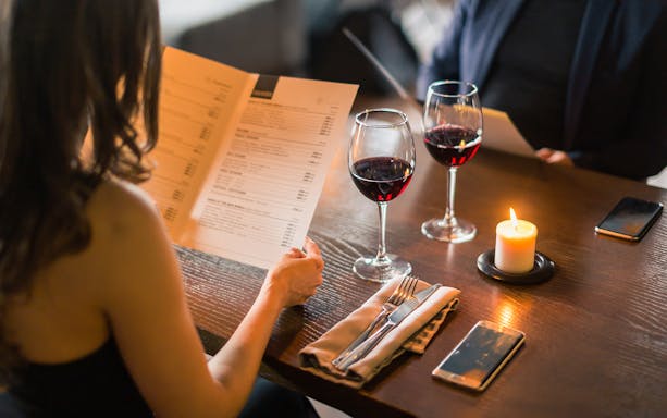 Couple reviewing menu with wine glasses and candle on Valentine's Day dinner cruise.