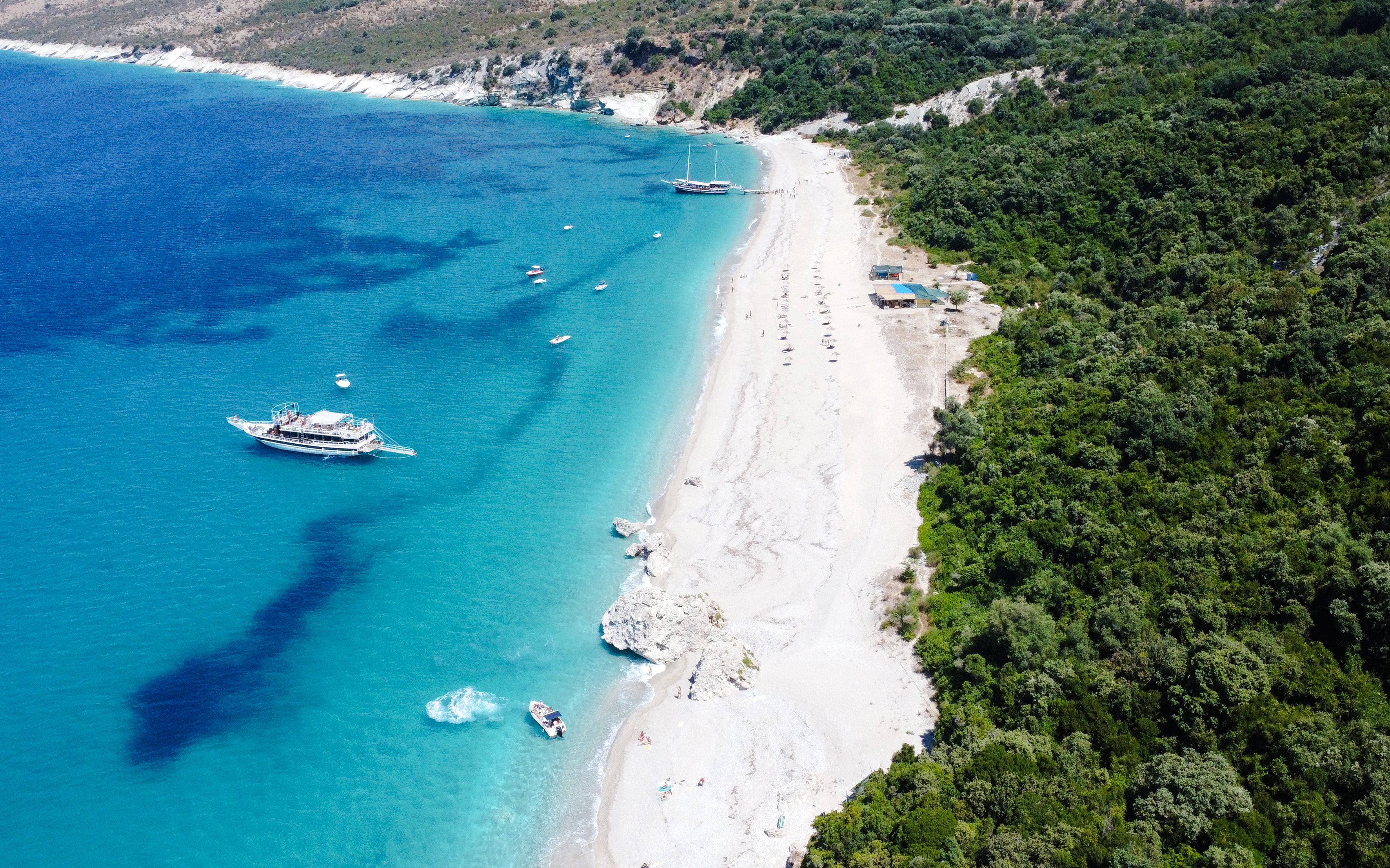 Aerial view of Krorëza Beach, Saranda, with boats on turquoise water and lush greenery.