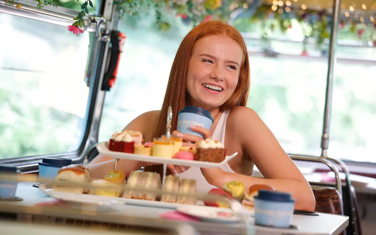 Woman enjoying afternoon tea with pastries on a vintage bus tour.