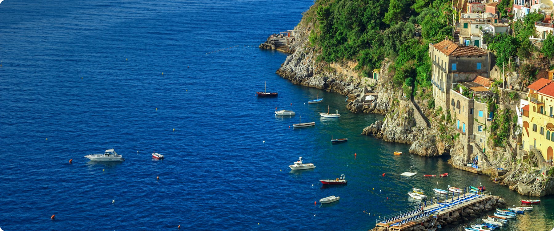 Boats anchored near rocky coastline and colorful buildings in Amalfi, Italy.