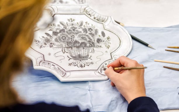 Artisan painting floral design on Royal Delft Blue pottery plate.