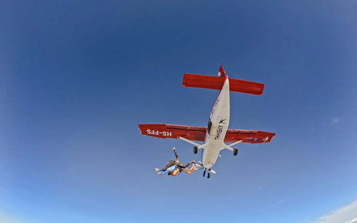 Skydivers jumping from a plane at 13000 ft against a clear blue sky.