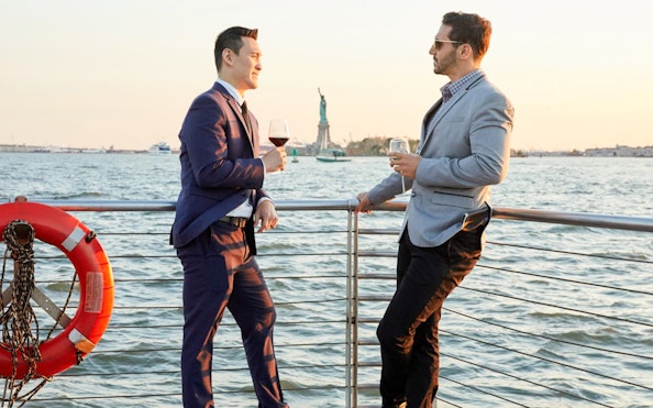 Two people enjoying drinks on a New York Bateaux lunch cruise with the Statue of Liberty in the background.