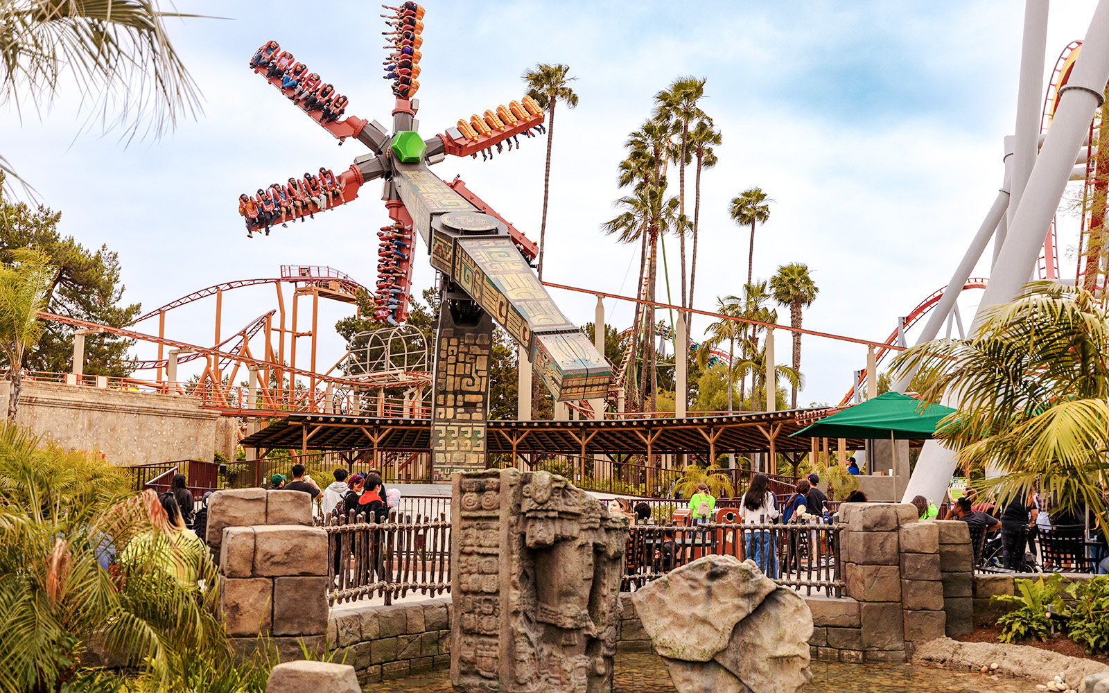 Sol Spin ride at Knott's Berry Farm with passengers in motion against a backdrop of palm trees and roller coasters.