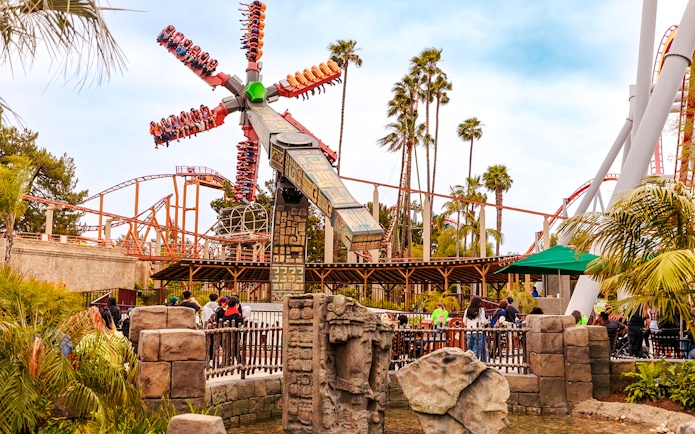 Sol Spin ride at Knott's Berry Farm with passengers in motion against a backdrop of palm trees and roller coasters.
