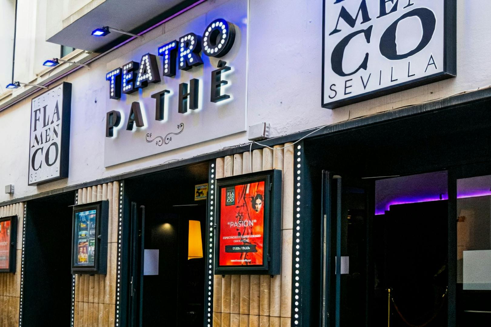 Entrance of Teatro Flamenco Sevilla with illuminated signs and posters.