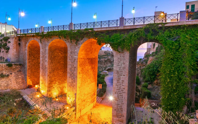 Stone bridge with arches illuminated at dusk in Polignano, Valle d'Itria, Italy.