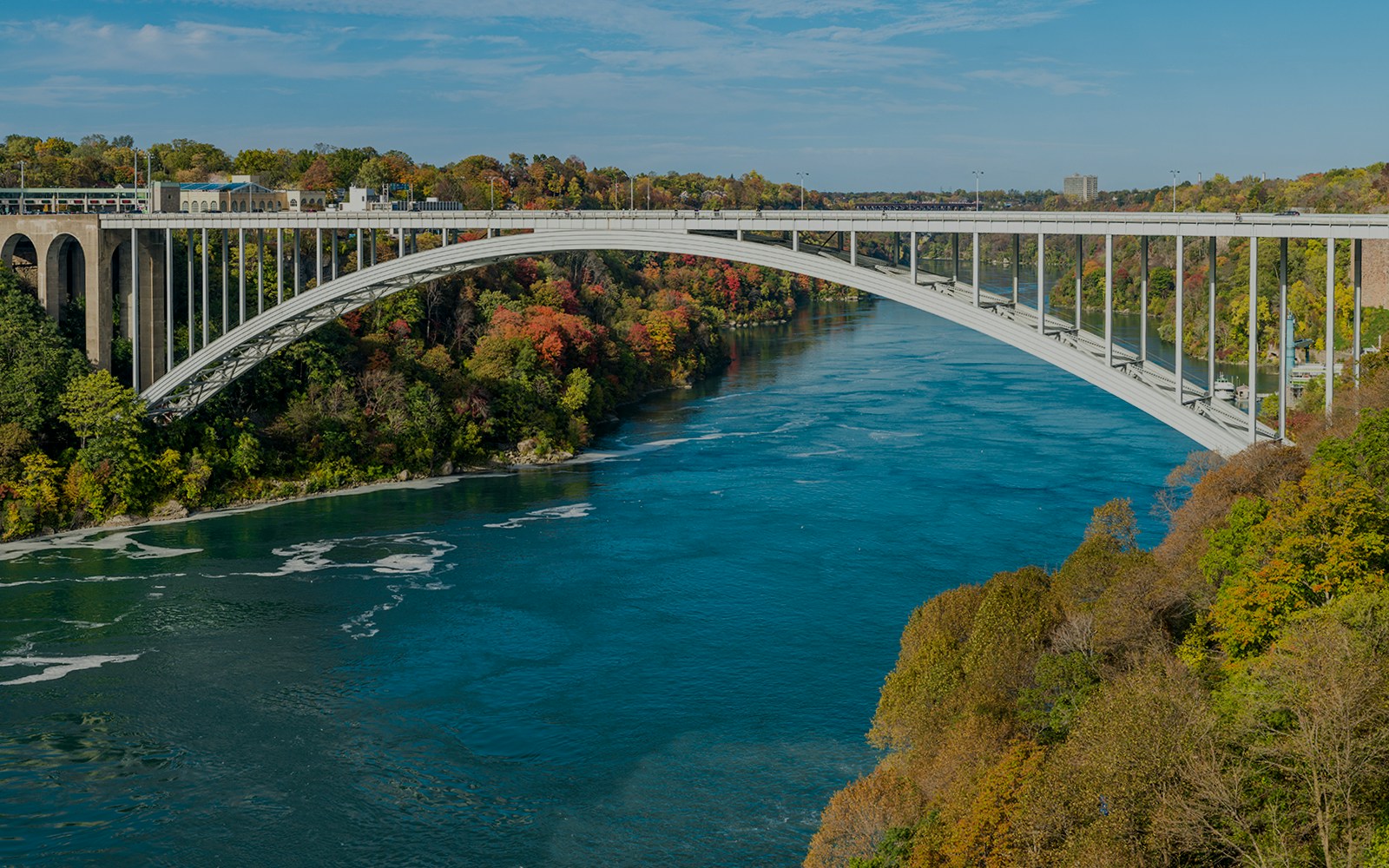 Rainbow Bridge spanning the Niagara River between USA and Canada, surrounded by autumn foliage.