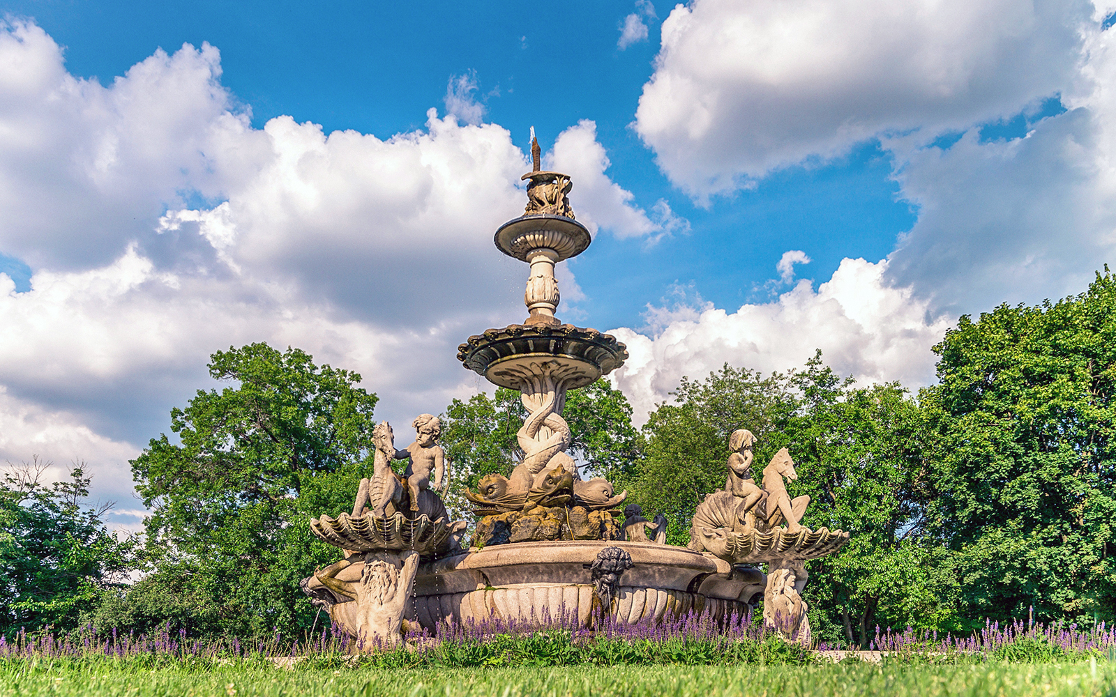 Fountain with sculptures at Bronx Zoo surrounded by trees and flowers.