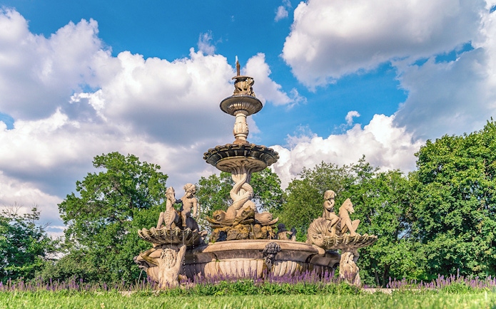 Fountain with sculptures at Bronx Zoo surrounded by trees and flowers.