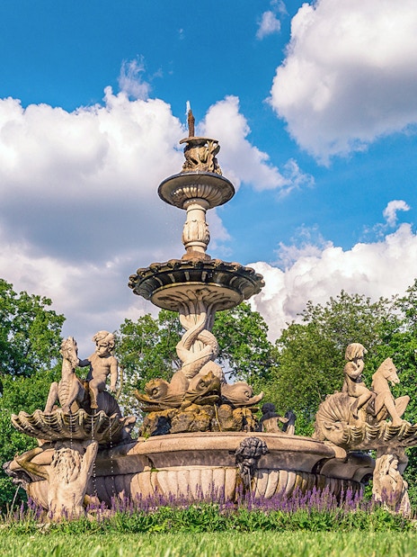 Fountain with sculptures at Bronx Zoo surrounded by trees and flowers.