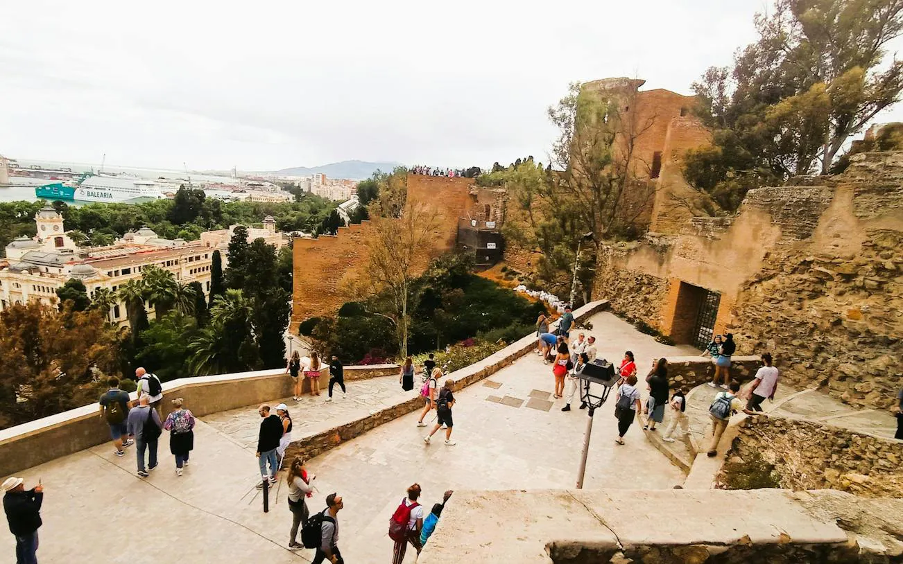 Malaga Alcazaba view with tourists exploring ancient fortress walls and cityscape in background.