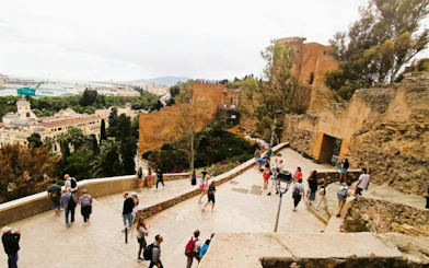 Malaga Alcazaba view with tourists exploring ancient fortress walls and cityscape in background.
