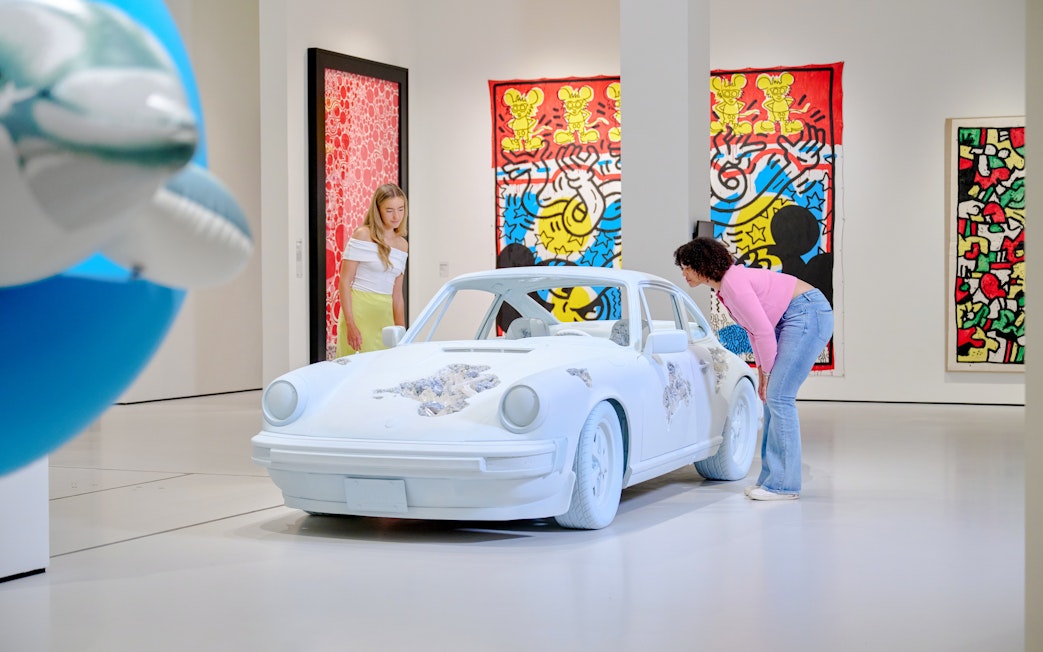 Visitors observing a car installation at Moco Museum London with colorful art in the background.