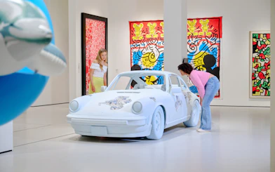 Visitors observing a car installation at Moco Museum London with colorful art in the background.