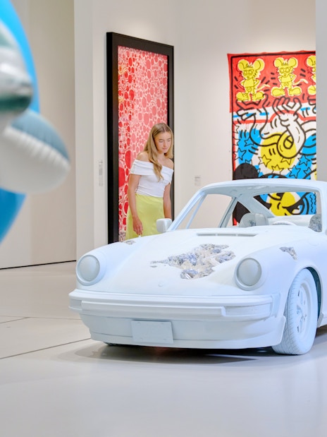 Visitors observing a car installation at Moco Museum London with colorful art in the background.