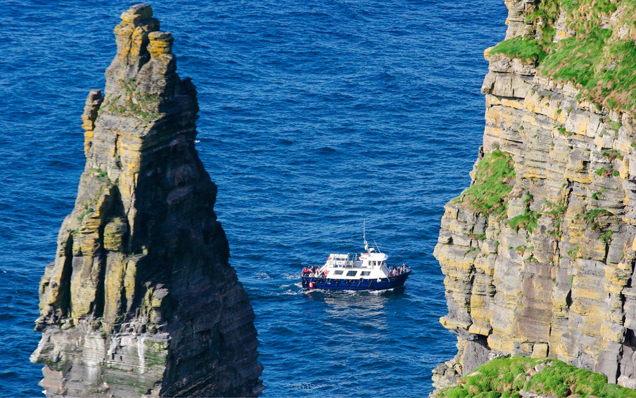 Boat tour approaching Cliffs of Moher, Ireland, with passengers viewing the dramatic coastal landscape.