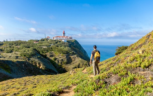 Traveler hiking towards Cabo da Roca lighthouse with Atlantic Ocean in the background.