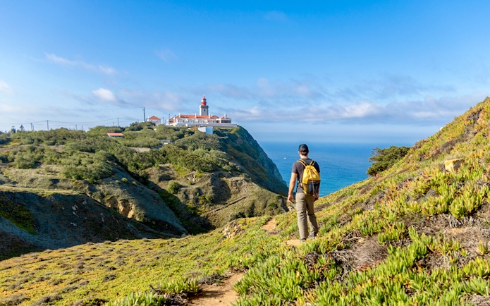 Traveler hiking towards Cabo da Roca lighthouse with Atlantic Ocean in the background.
