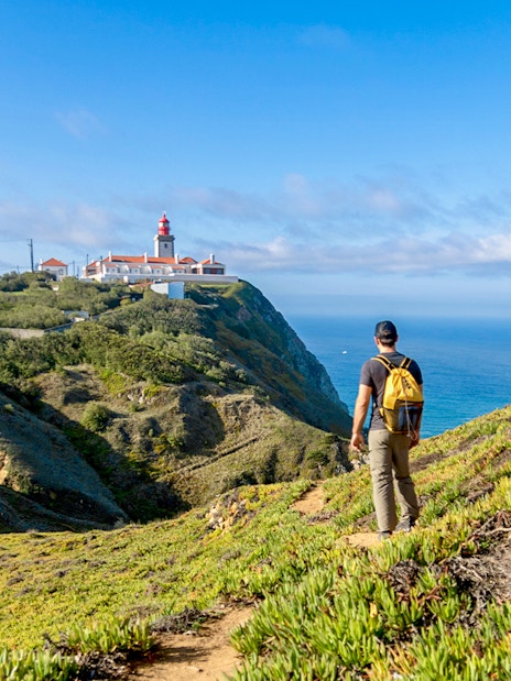 Traveler hiking towards Cabo da Roca lighthouse with Atlantic Ocean in the background.