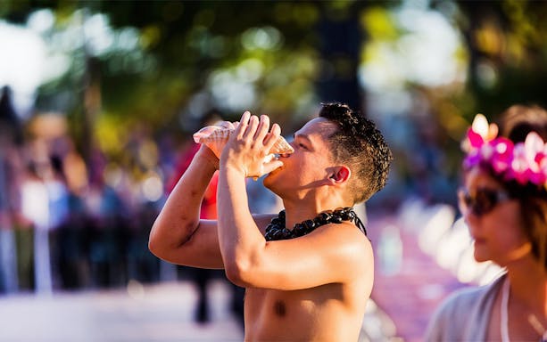 Blowing conch shell to start ceremonies at Paradise Cove Luau, Hawaii.