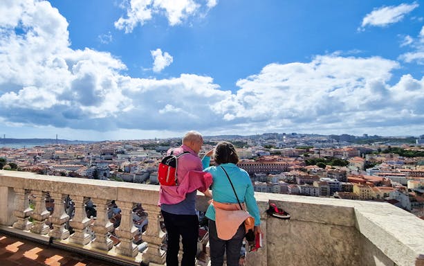 Two people overlooking Lisbon cityscape from a viewpoint.
